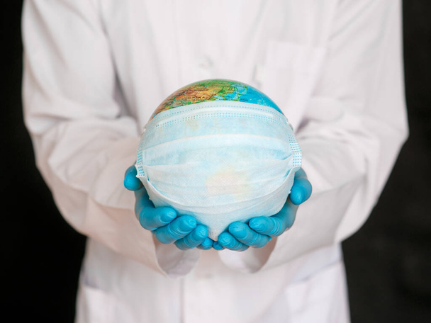 globe with a medical mask from covid-19 virus in hands ofdoctor close-up. concept epidemic and pandemic of Coronavirus. - Photo, Image