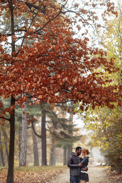 glückliches gemischtrassiges Paar spaziert im Herbstpark, schwarzer Mann und weiße rothaarige Frau - Foto, Bild