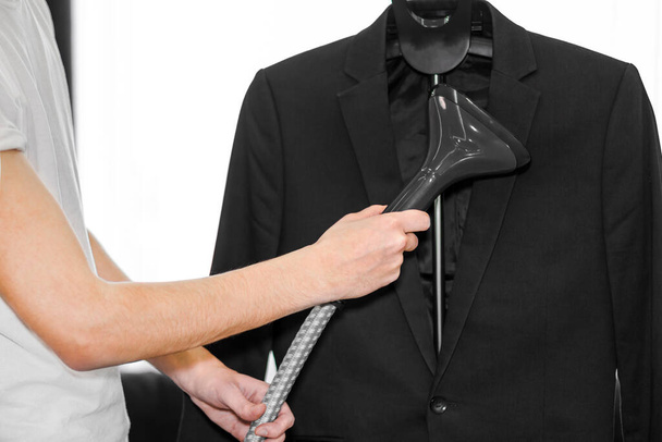 a man puts things in order. holds the garment steamer in his hand and smoothes the jacket after washing - Foto, Imagen
