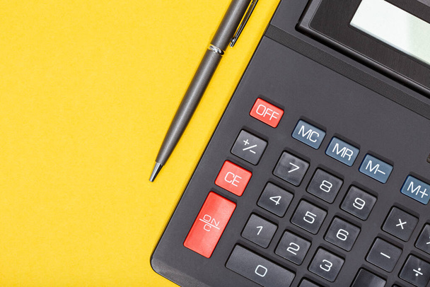 Calculadora y pluma sobre fondo amarillo. Antecedentes económicos o empresariales
 - Foto, imagen