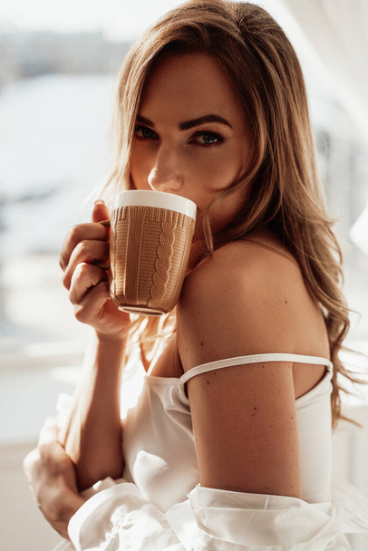 Graceful young woman in lingerie posing with a cup of coffee over the white background - Foto, Imagen