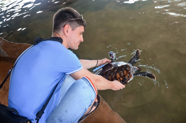 Jeune homme brune avec caméra relâche la tortue dans l'eau, volontaire sauve les tortues, protection des animaux, garçon prend des photos de la tortue. sauver les animaux Centre de recherche sur la conservation de la mer à Bento
 - Photo, image