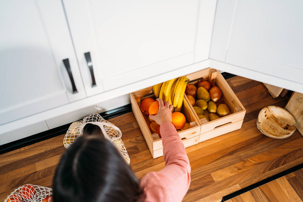Top view of a Woman keeping the purchase of fruit in her kitchen. Using a reusable organic cotton mesh bag on wooden background. Zero waste, plastic free concept. Sustainable lifestyle. - Photo, Image
