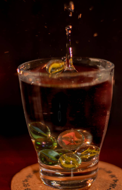 stříkance kapek ve sklenici vody a kuličky nebo barvy skleněné kuličky - Fotografie, Obrázek