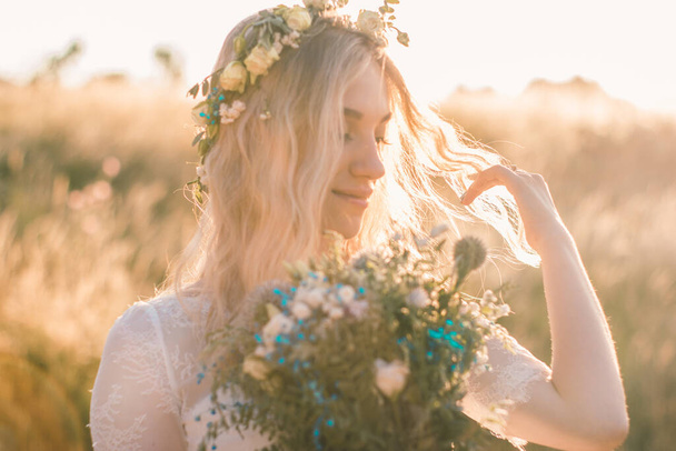 フィールドで夏に花の花輪とボーホスタイルの白いドレスで美しい若い女性の肖像画。選択的ソフトフォーカス. - 写真・画像