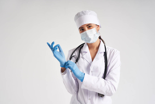 Młody lekarz zakładający rękawiczki chirurgiczne na białe tło - Zdjęcie, obraz