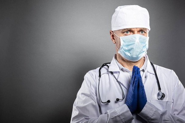 Müder frustrierter Arzt in medizinischer Schutzmaske betet. - Foto, Bild