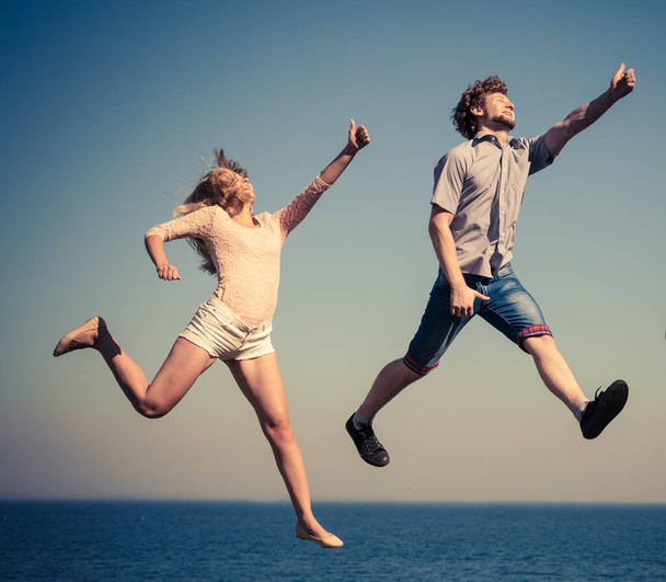 Carefree young couple friends jumping by sea ocean water. Happy woman and man having fun. Summer happiness and freedom. - Foto, Imagem