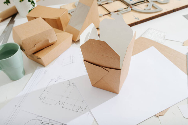 Messy workplace for designing cardboard boxes in a private workshop. Rulers, sheets, boxes and special board with a cutting form. - Foto, Imagen