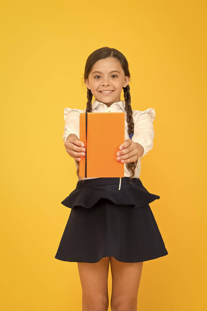Love reading for pleasure. Cute small schoolchild holding reading book on yellow background. Adorable little girl learn reading at primary school. Reading develops the mind, copy space - Photo, image