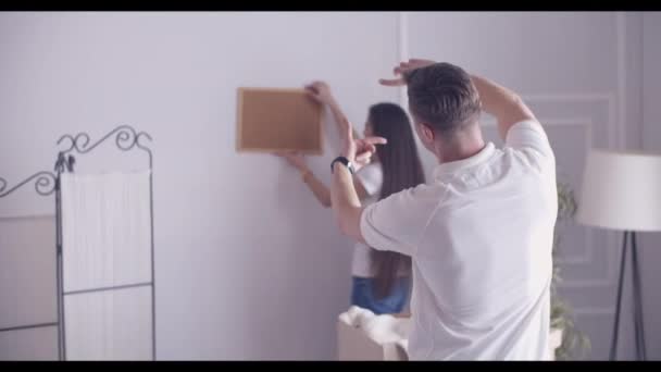 Mann und Frau hängen während des Umzugs Bilder an ihren Wohnort - Filmmaterial, Video
