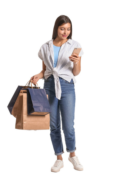 Jonge vrouw met mobiele telefoon en boodschappentassen op witte achtergrond - Foto, afbeelding