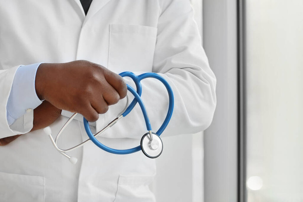 Male African-American doctor with stethoscope near window in clinic, closeup - Photo, Image