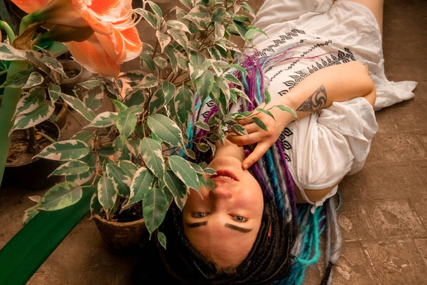 gyönyörű szexi lány többszínű raszta fehér ruhában fekszik a földön egy narancssárga lépcső alatt a növények között, arc, nagy portré. Üvegház egzotikus trópusi növények a botanikus kert Ukrajnában, Dnipr - Fotó, kép