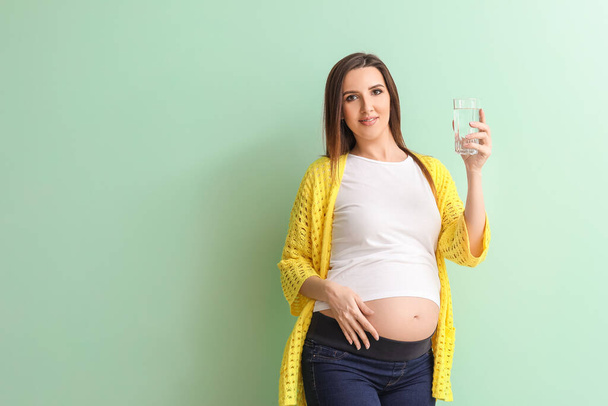 Красивая беременная женщина со стаканом воды на цветном фоне
 - Фото, изображение