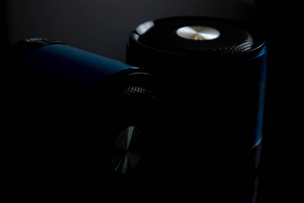 two bluetooth speakers in blue standing on black glass, closeup in low key - Foto, afbeelding