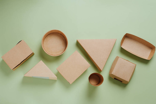 Ekologiczne jednorazowe papierowe pudełka żywności o wszystkich kształtach na zielonym tle. Widok z góry. - Zdjęcie, obraz