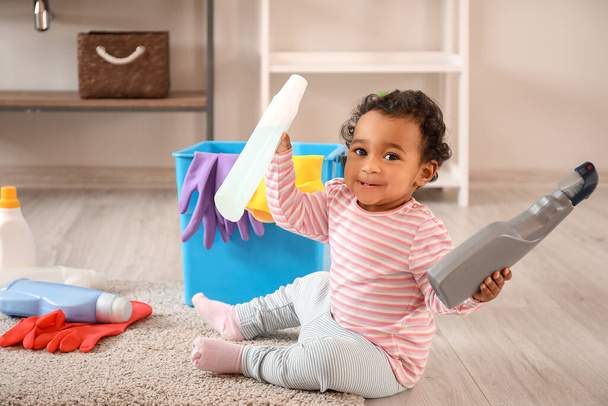 Pequeño bebé afroamericano jugando con artículos de limpieza en casa. Niño en peligro
 - Foto, imagen