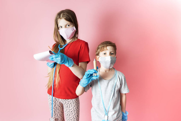 Personal protective equipment: children a boy and a girl in medical masks and blue gloves are playing with a childrens set of a doctor. - Фото, изображение