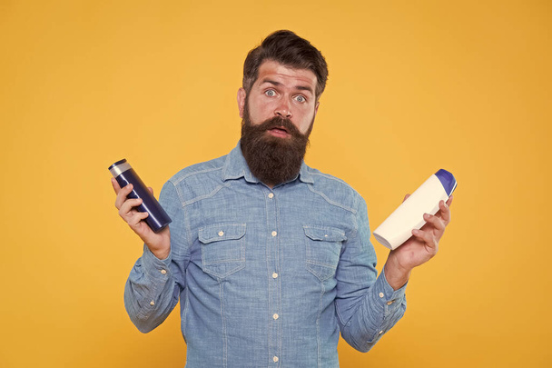 Which soap best. Bearded man hold soap bottles yellow background. Hipster choose liquid soap. For washing in bath or shower. Skincare and health. Grooming and hygiene. Soap cleanser for male skin - Photo, image