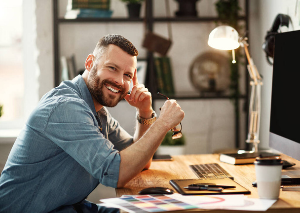 Щасливий молодий чоловік у повсякденному одязі та окулярах працює за комп'ютером, сидячи з кавою на робочому місці з великим моніто
 - Фото, зображення