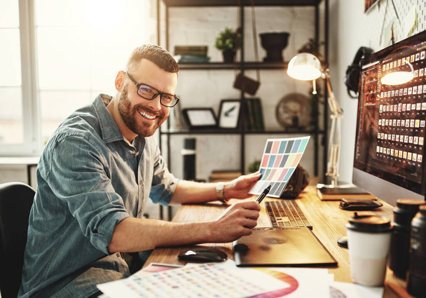 Hombre joven feliz en ropa casual y gafas trabajando en la computadora mientras está sentado con café para llevar en el lugar de trabajo con un gran monito
 - Foto, Imagen