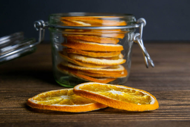 Dried oranges in a jar and on a dark wooden table next to the jar. Close-up. - Photo, Image