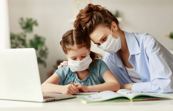 Exhausted woman in medical mask sitting at table and watching diligent girl writing in notebook while doing homework together during pandemi - Photo, Image