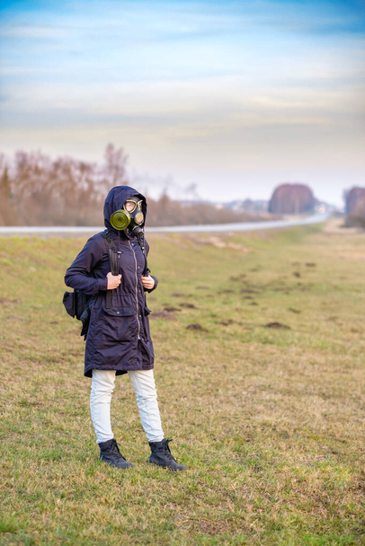 A girl in a gas mask travels hitchhiking. - Zdjęcie, obraz