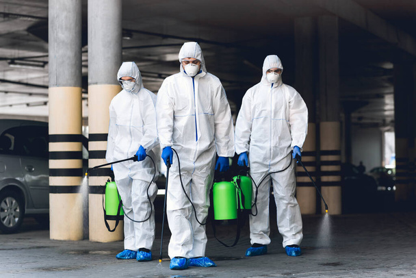 Wirusolodzy noszący kombinezony ochronne dezynfekujące parking rozpylonymi chemikaliami - Zdjęcie, obraz