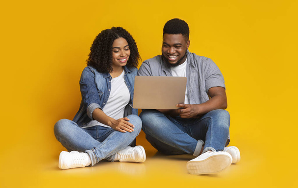 Positiva coppia nera seduta sul pavimento con computer portatile, guardando film insieme
 - Foto, immagini
