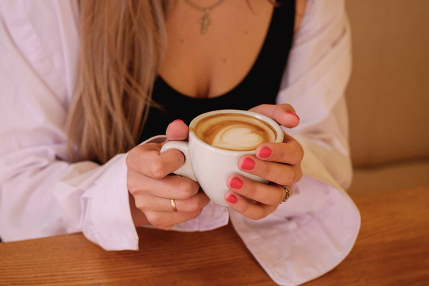 Seksowna dziewczyna siedząca przy stole i pijąca kawę. singielka w białej męskiej koszuli - Zdjęcie, obraz