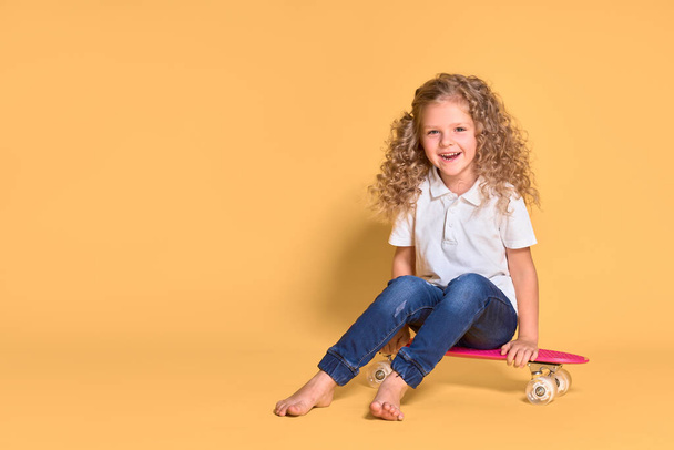 Active and happy girl with curly hair, headphones having fun with penny board, smiling face stand skateboard. Penny board cute skateboard for girls. Lets ride. Girl with penny board yellow background - Zdjęcie, obraz