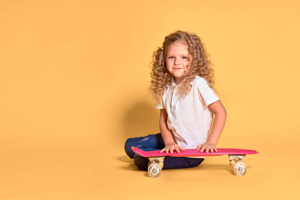 Active and happy girl with curly hair, headphones having fun with penny board, smiling face stand skateboard. Penny board cute skateboard for girls. Lets ride. Girl with penny board yellow background - Photo, Image