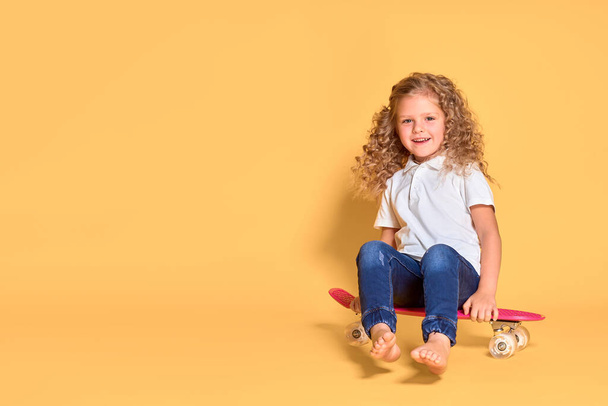 Active and happy girl with curly hair, headphones having fun with penny board, smiling face stand skateboard. Penny board cute skateboard for girls. Lets ride. Girl with penny board yellow background - Foto, imagen