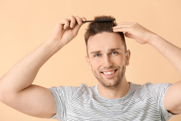 Hezký mladý muž česání vlasy na barevném pozadí - Fotografie, Obrázek