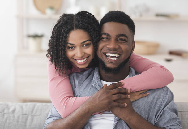 Kochająca afro-amerykańska para przytulająca się w domu i patrząca w kamerę - Zdjęcie, obraz