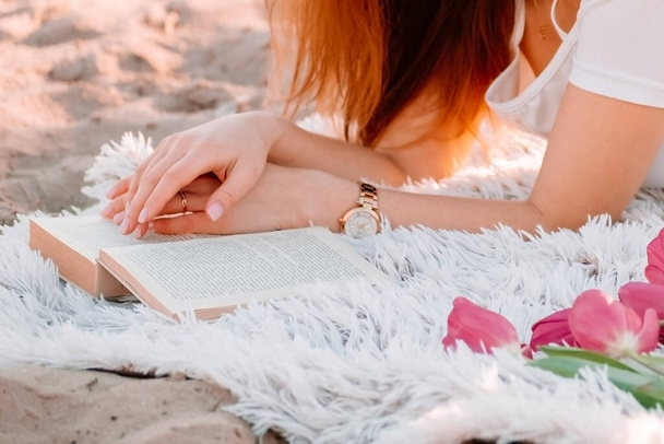 Piękna jasnowłosa dziewczyna leży na kratę i czyta książkę. Romantyczne śniadanie o świcie, letni poranek. sesja zdjęciowa z pączkami i kwiatami tulipany - Zdjęcie, obraz