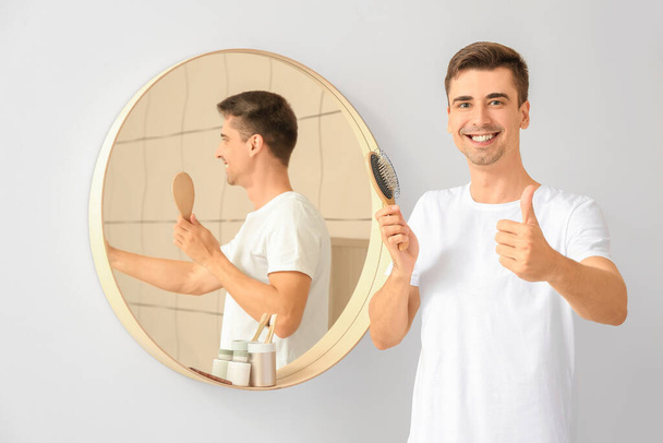 Όμορφος νεαρός άνδρας βουρτσίζει τα μαλλιά στο σπίτι - Φωτογραφία, εικόνα