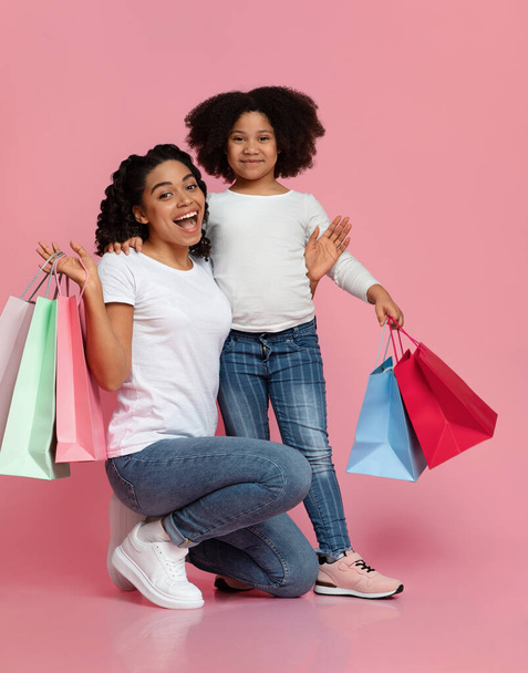Heyecanlı Afro-Amerikalı anne ve küçük kızı alışveriş paketleriyle poz veriyorlar. - Fotoğraf, Görsel