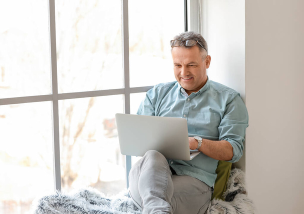 Mature man using laptop at home - Фото, изображение
