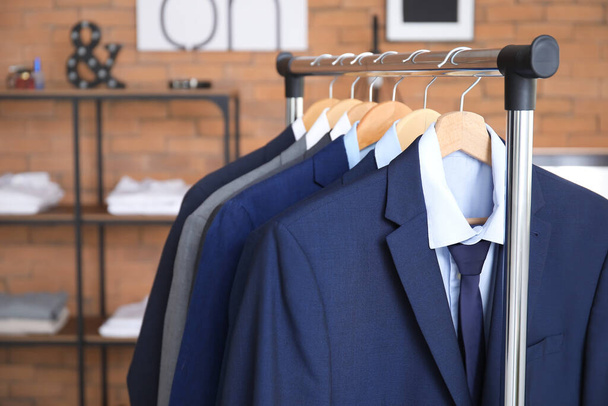 Hanger with different stylish male suits in store - Foto, Bild