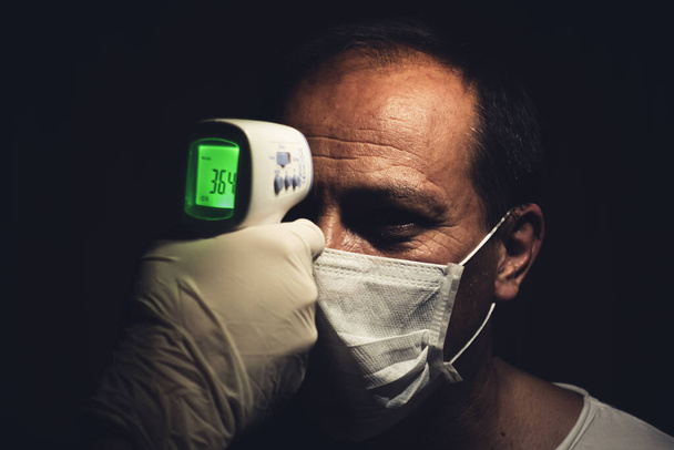 Close-up opname van een infrarood thermometer die de normale lichaamstemperatuur van een gezonde oudere man voor het coronavirus meet - Foto, afbeelding