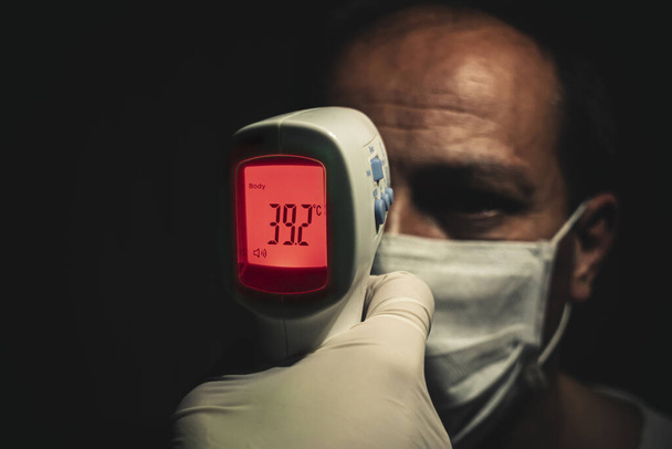 Ujęcie z bliska termometru na podczerwień mierzącego niebezpiecznie wysoką temperaturę ciała starszego mężczyzny z gorączką - Zdjęcie, obraz