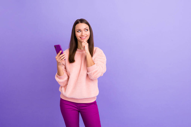 Photo of pretty addicted blogger lady hold telephone thinking over creative new post text idea minded wear casual fur fluffy pullover pants isolated purple color background - Valokuva, kuva