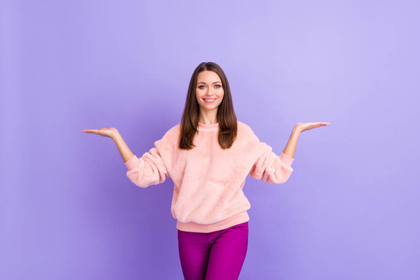 Photo of attractive lady holding novelty product on open arms presenting two option offer variants wear casual fur fluffy pullover pants isolated purple color background - Фото, зображення