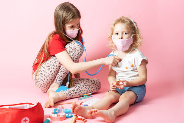 Personal protective equipment: masked sisters play a doctor and a teenager girl listens to the breathing of her younger sister. - Φωτογραφία, εικόνα