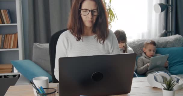 Confident lady in eyewear working on laptop with children - Felvétel, videó