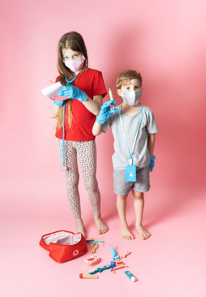 Personal protective equipment: children a boy and a girl in medical masks and blue gloves are playing with a childrens set of a doctor. - Foto, afbeelding