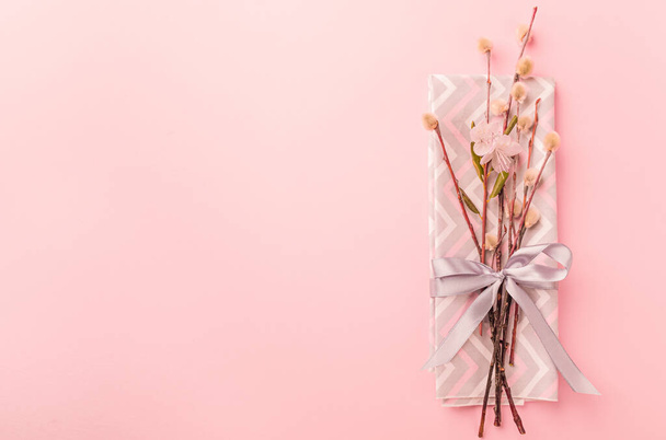 Ивовые ветки празднично завязаны салфеткой с атласной лентой с бантом на пастельно-розовом. Праздничная весенняя концепция
 . - Фото, изображение
